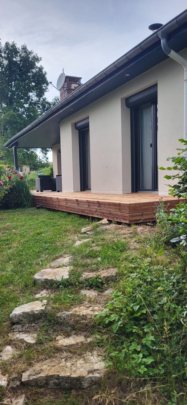 Terrasse en bois devant une maison avec jardin verdoyant et arbustes.