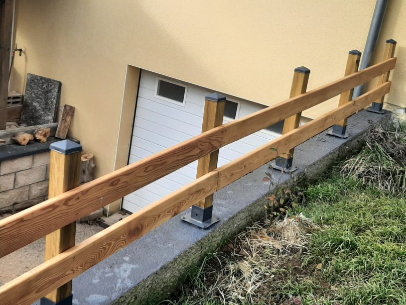 Rambarde en bois sur un muret, avec un garage en arrière-plan.