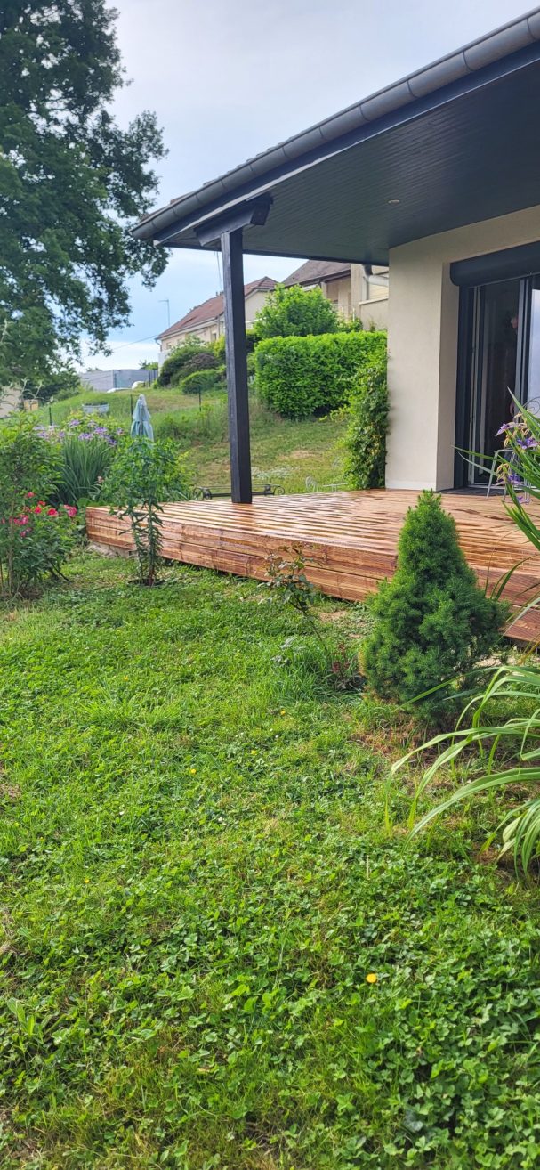Terrasse en bois devant une maison avec jardin verdoyant et arbustes.