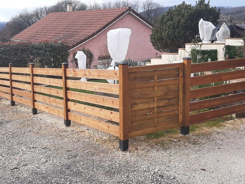 Clôture en bois avec poteaux et capuchons noirs entourant une propriété.