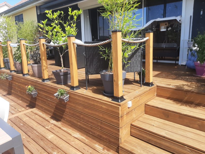 Terrasse en bois tropical avec des poteaux, plantes en pots et rampes décoratives.